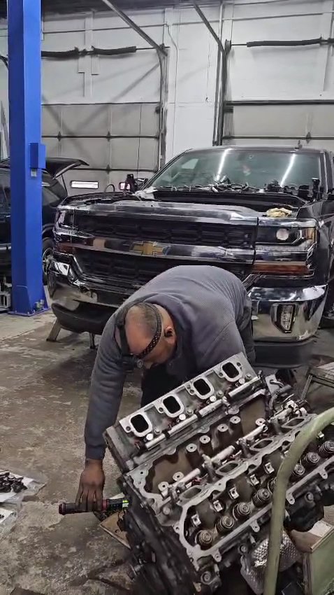 Technician working on a cylinder head beside a pickup truck