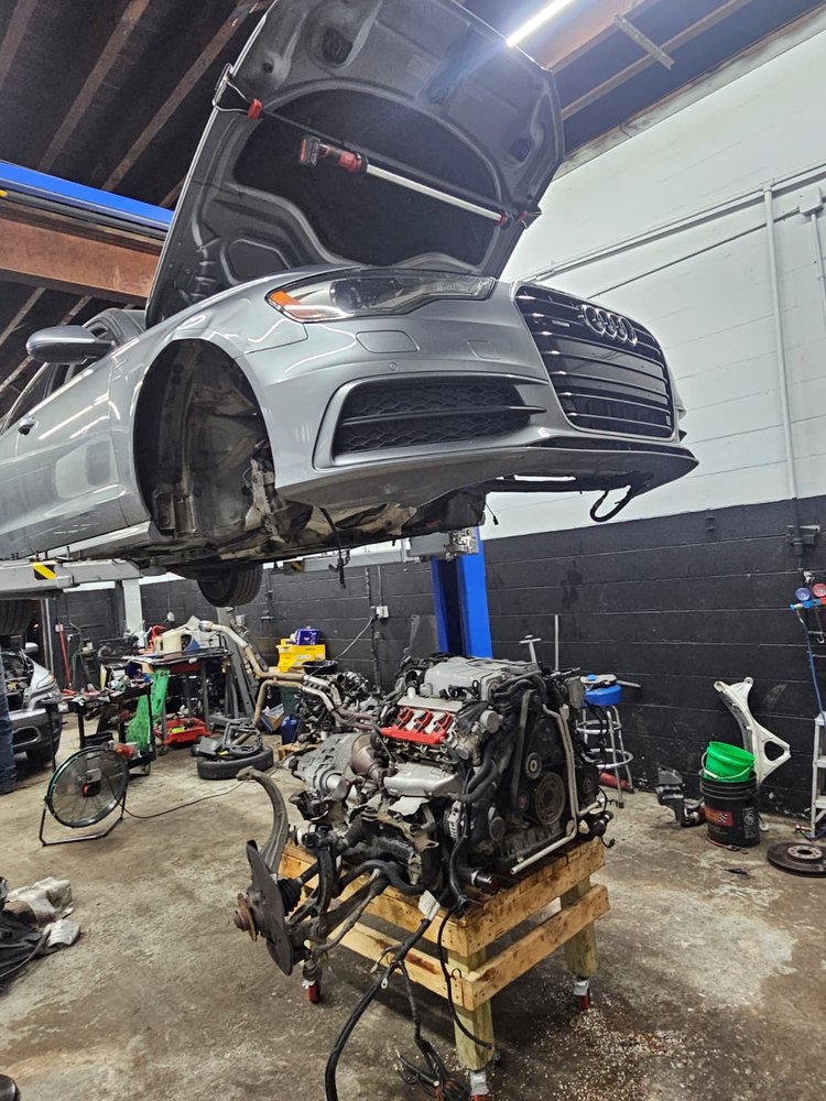 Sedan on a lift beside an engine on a stand, Milwaukee shop