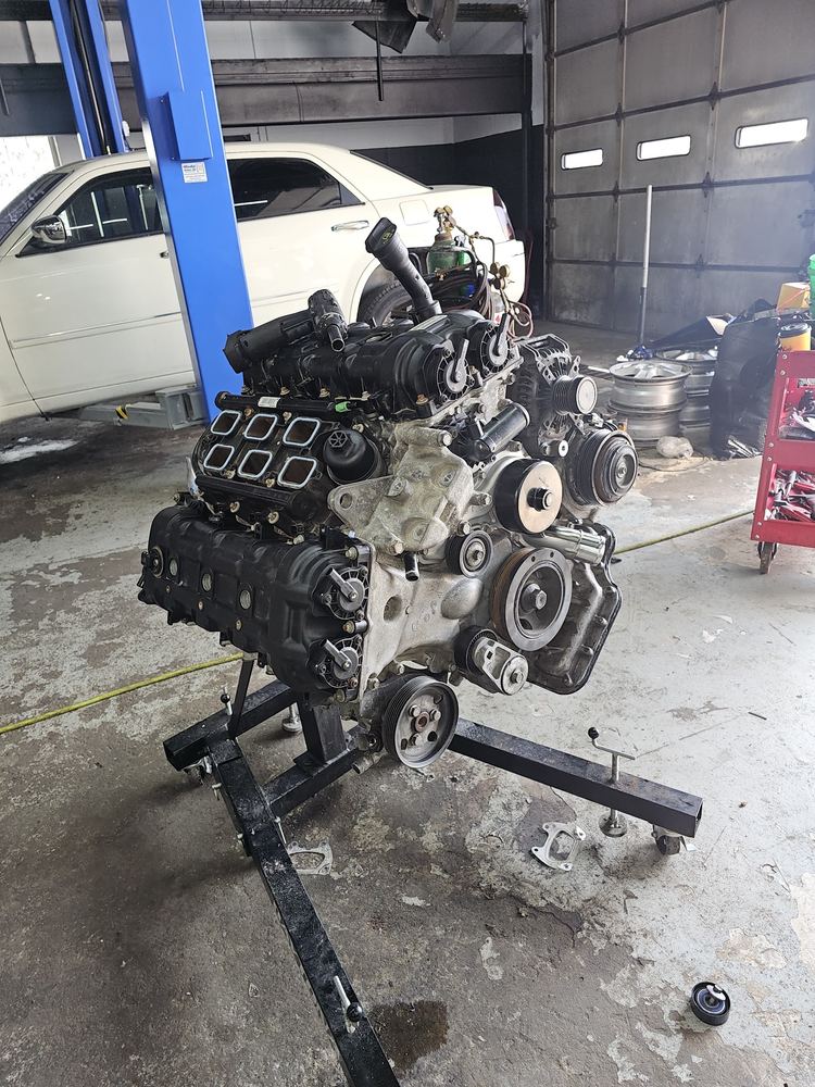 Engine on a stand next to a white sedan in the bay